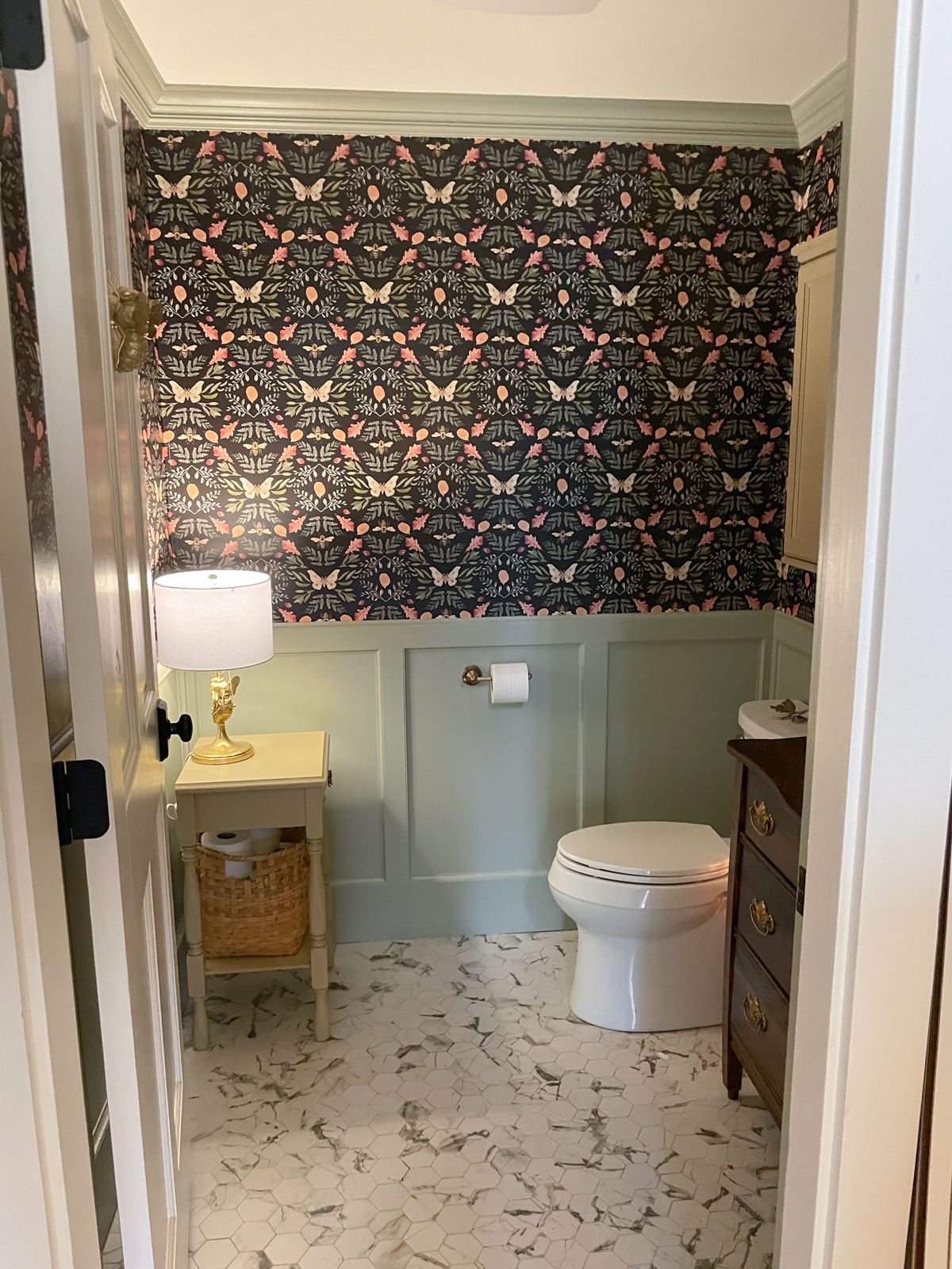Half bathroom with green wainscoting and peel and stick wallpaper charming side table with bee lamp